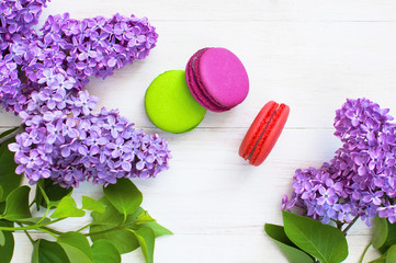 Sweet colorful french macaroons and spring lilac flowers on white wooden background. Beautiful dessert Colorful almond cookies Pastel colors Bouquet of lilacs