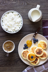 Cottage cheese pancakes (syrniki) with sour cream, orange jam and fresh blueberries on a plate. Breakfast or lunch concept. 
