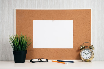 Blank paper note on cork board with golden alarm clock, reading glasses, pen and green plant in pot. memo and time management concept. blank note for copy space or typography