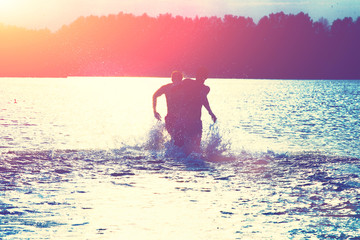 Glückliche junge Menschen laufen und springen am See beim Sonnenuntergang