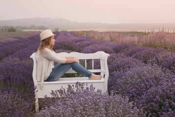 Beautiful young woman wearing a hat is sitting on a bench on the lavender field