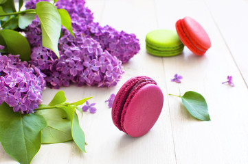 Sweet colorful french macaroons and spring lilac flowers on white wooden background. Beautiful dessert Colorful almond cookies Pastel colors Bouquet of lilacs