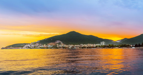 Golden sunset on Adriatic sea with reflection on water, view on Budva city and mountains in Montenegro