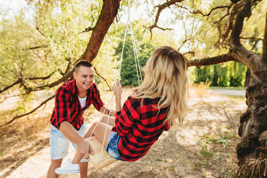 A loving couple on a swing near a tree. Fun and laughter. The girl swinging on a swing, and boyfriend pushing her.