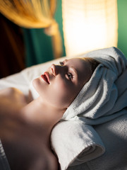 Young woman getting spa treatment in salon, lying on the table with a tovel on head and looking...