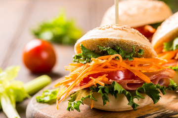 Homemade mini burgers with ham, tomato, carrot, fresh salad served on wooden board. Healthy junk food concept with copy space.