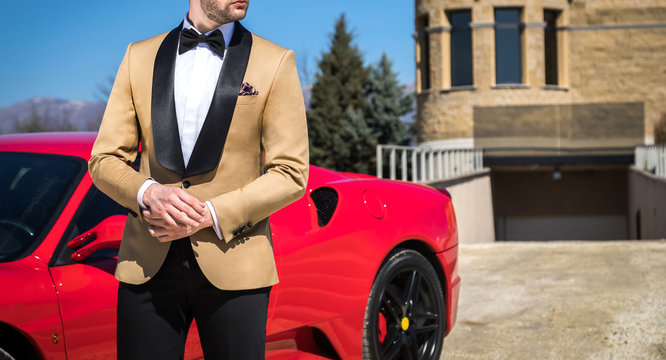 Man in custom tailored tuxedo, suit posing outdoors in front of expensive car