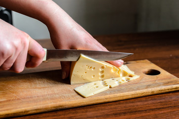 Slicing cheese on a wooden board. Preparation of products for storage in the refrigerator.