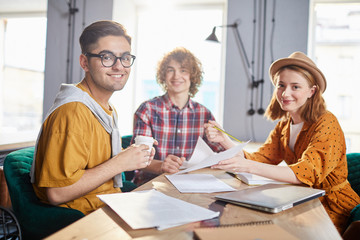 Obraz premium Three young successful employees looking at camera while discussing papers in office