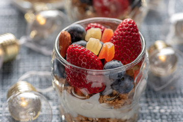 A healthy colourful snack consisting of granola and yoghurt with assorted berried and dried fruits in a small glass cup.

