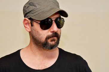 Obraz premium Side view portrait of a stylish bearded man wearing sunglasses and a cap, looking away with a calm and confident expression