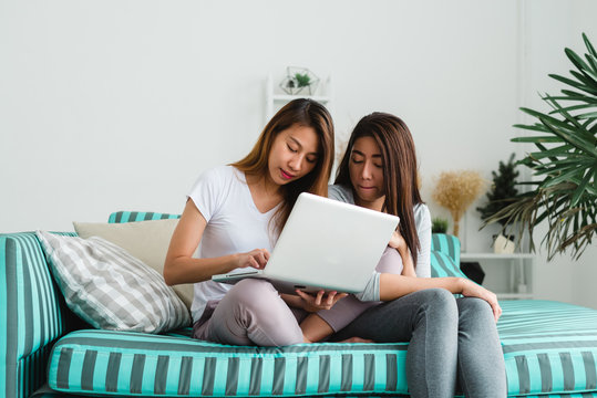 Beautiful young asian women LGBT lesbian happy couple sitting on sofa buying online using laptop a computer and credit card in living room at home. LGBT lesbian couple together indoors concept.