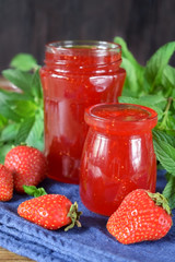 Strawberry jam in glass jars surrounded by the berries and mint
