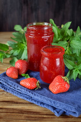 Strawberry jam in glass jars surrounded by the berries and mint