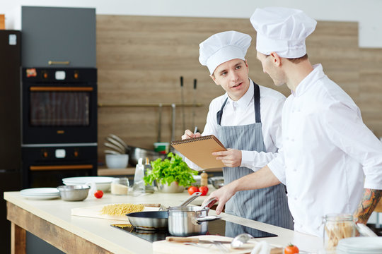 Young man consulting about cooking procedure with chef in the kitchen