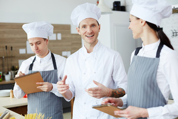 Happy young chef giving advice to his trainees during process of cooking