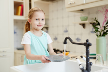 Little girl washing her plate over sink in the kitchen after eating