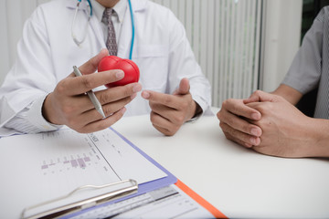 Doctor and patient are discussing for heart disease with young man patient and making notes while sitting at medical consultation.