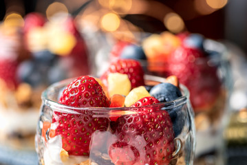 A healthy colourful snack consisting of granola and yoghurt with assorted berried and dried fruits in a small glass cup.


