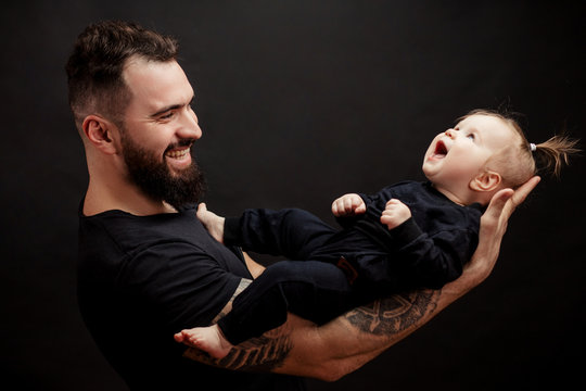 Adorable portrait of happy masculine father holding his little beautiful daugter over black background.