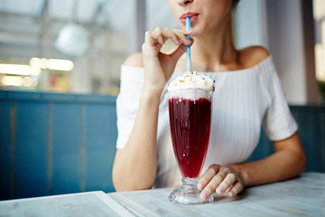Berry drink with whipped Chantilly top in long glass and young female enjoying it