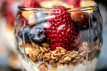 A healthy colourful snack consisting of granola and yoghurt with assorted berried and dried fruits in a small glass cup.

