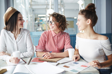 Young students gathered by table in cafe to discuss assignment and prepare for seminar
