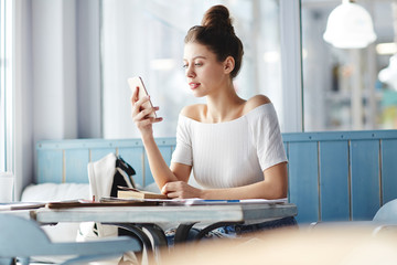 Contemporary young woman with smartphone searching in the net or messaging in social networks