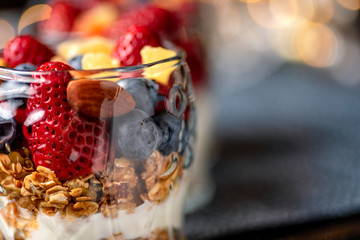 A healthy colourful snack consisting of granola and yoghurt with assorted berried and dried fruits in a small glass cup.

