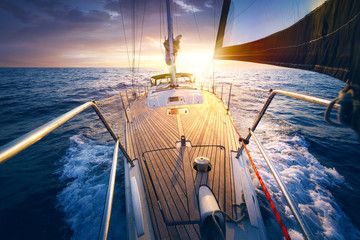 Sunset at the Sailboat deck while cruising / sailing at opened sea. Yacht with full sails up at the end of windy day. Sailing theme - background. Yachting design. - obrazy, fototapety, plakaty