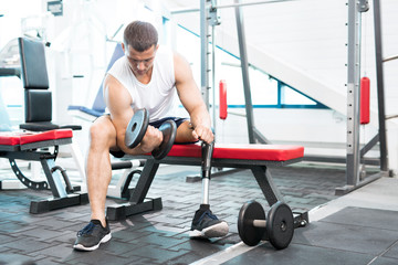 Young disabled man with dumbbells training in gym