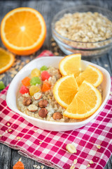 Homemade oatmeal porridge with orange, candied fruit and hazelnut on grey wooden background. Healthy breakfast.