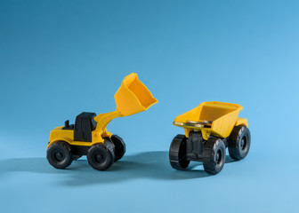 Yellow toy bulldozer loading money to the yellow toy truck. Space for text placement. 