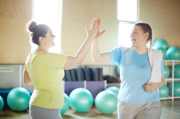Two active oversized women making high five after successful training in gym