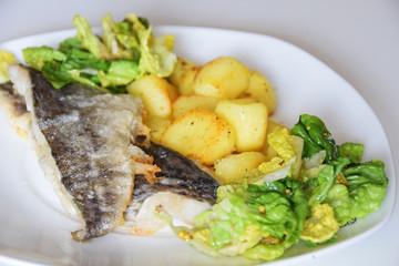 fried cod fish, baked potatoes in a pan, green lettuce with spices,