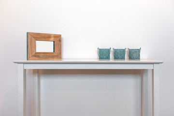 Empty picture frame with three decorative candle holders on white side table against white wall with copy space