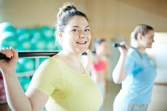 Happy young plus-sized woman and her friend exercising with gymnastic bars