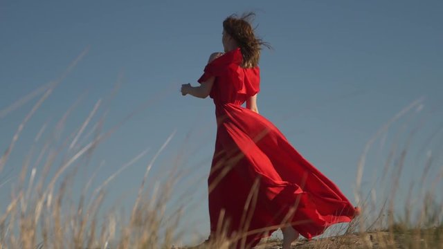 young female model in scarlet flowing in the wind dress and barefoot posing
