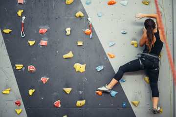 Sporty young woman training in a colorful climbing gym. Free climber girl climbing up indoor