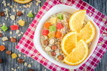 Homemade oatmeal porridge with orange, candied fruit and hazelnut on grey wooden background. Healthy breakfast.