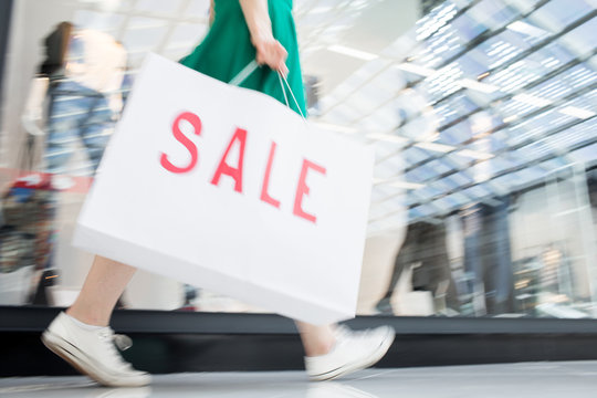Close-up of unrecognizable teenage girl carrying large shopping bag with Sale inscription while walking over mall and finding best offers