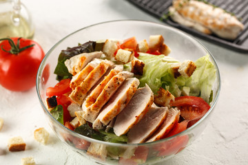 salad cesar with chicken grill in glass bowl on white wooden table. Decor fresh vegetables