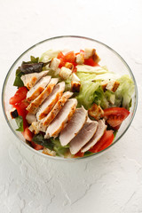 salad cesar with chicken grill in glass bowl on white table. Top view. Flat lay. Copyspace