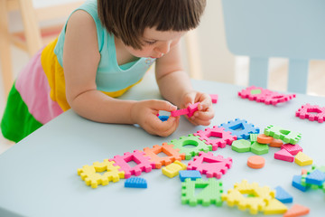 little girl playing at a children's table with a puzzle, early education. Bright soft blocks