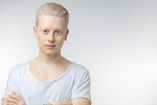 Portrait of blonde young man with uncommon appearance wears white t shirt, looking at camera, isolated over white studio background with copyspace for text.