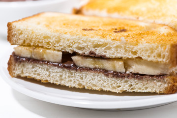 sweet sandwich with chocolate paste and banana on white table, closeup