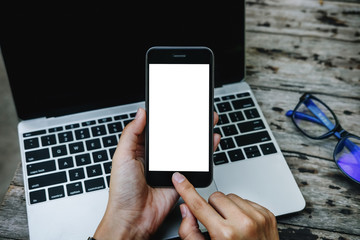 man hand holding empty or blank screen of smartphone with laptop computer. mobile can be add your texts or others. clipping path at white space.