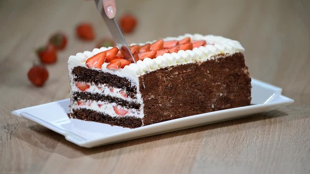 Cutting with a knife chocolate cake with strawberries.