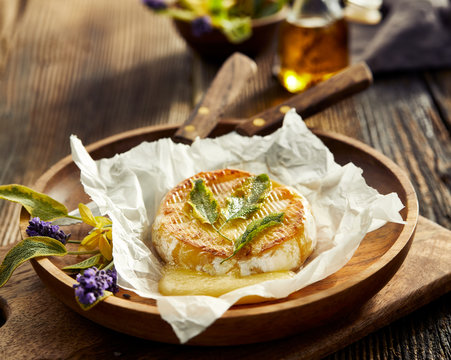 Grilled camembert cheese with addition of herbs on a wooden plate