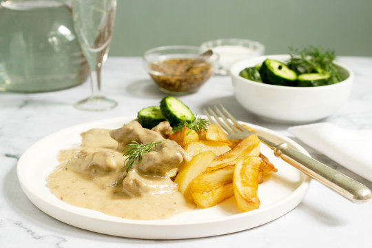 Beef Stroganoff traditional Russian dish of beef in sauce, served with fried potatoes, canned cucumbers, vodka.